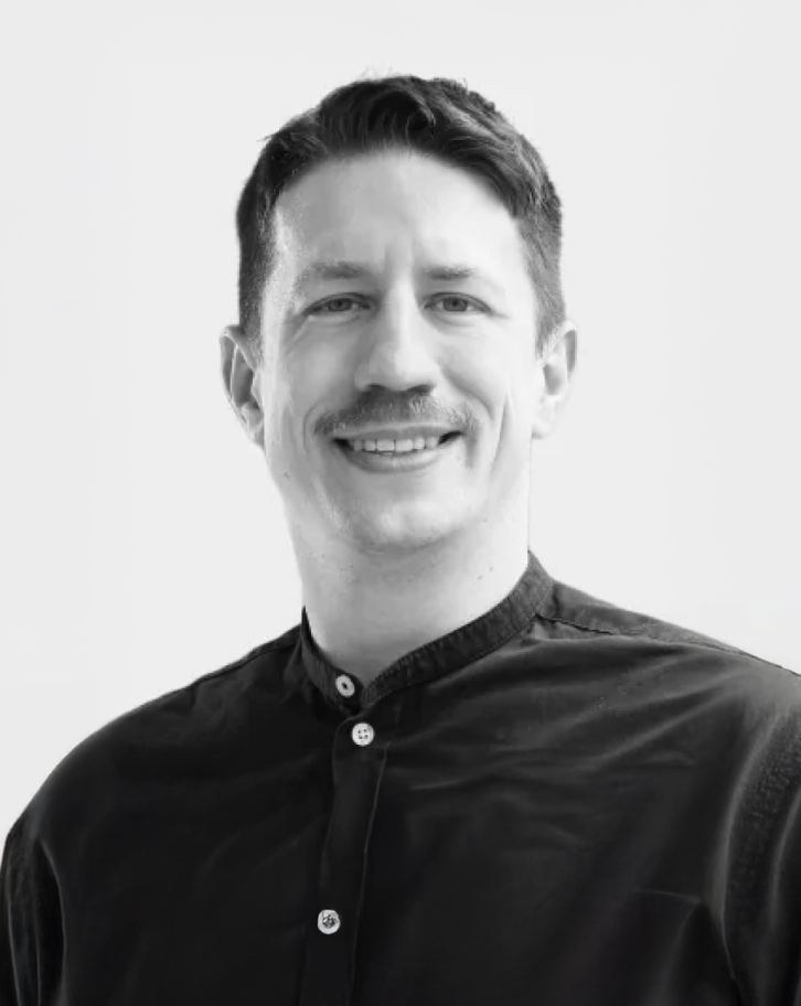 Black and white portrait of Bernhard Kratzwald wearing a dark mandarin collar shirt
