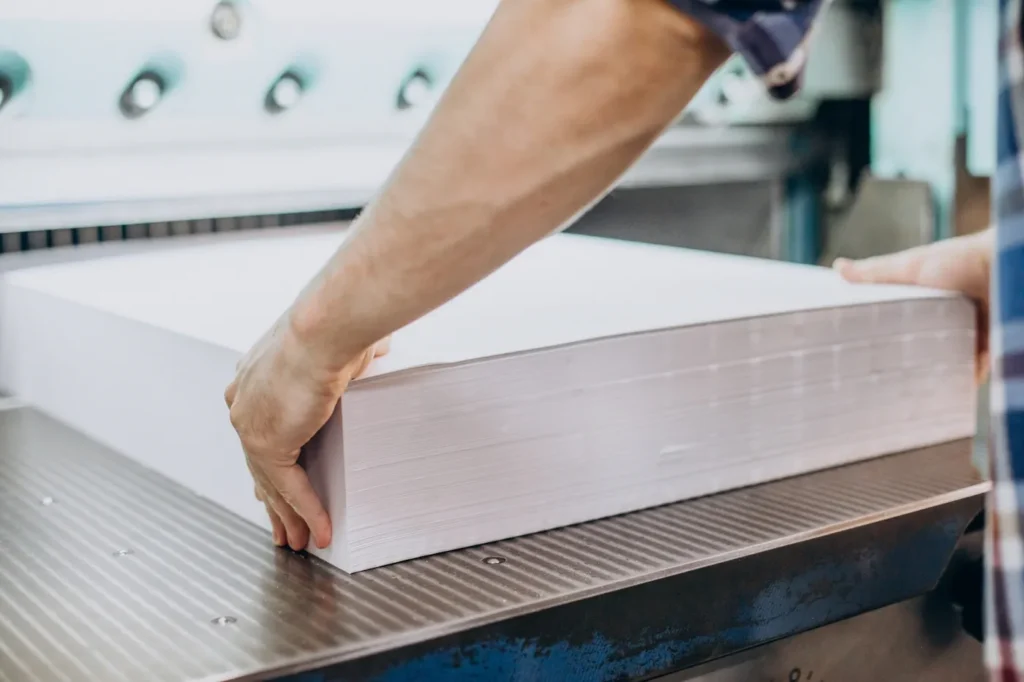 Closeup photo of a worker handling a large stack of neatly cut white paper 